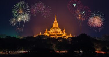 Templo budista iluminado com luzes douradas e fogos estourando no céu