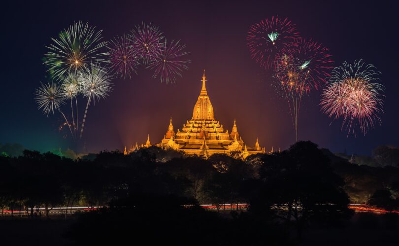 Templo budista iluminado com luzes douradas e fogos estourando no céu