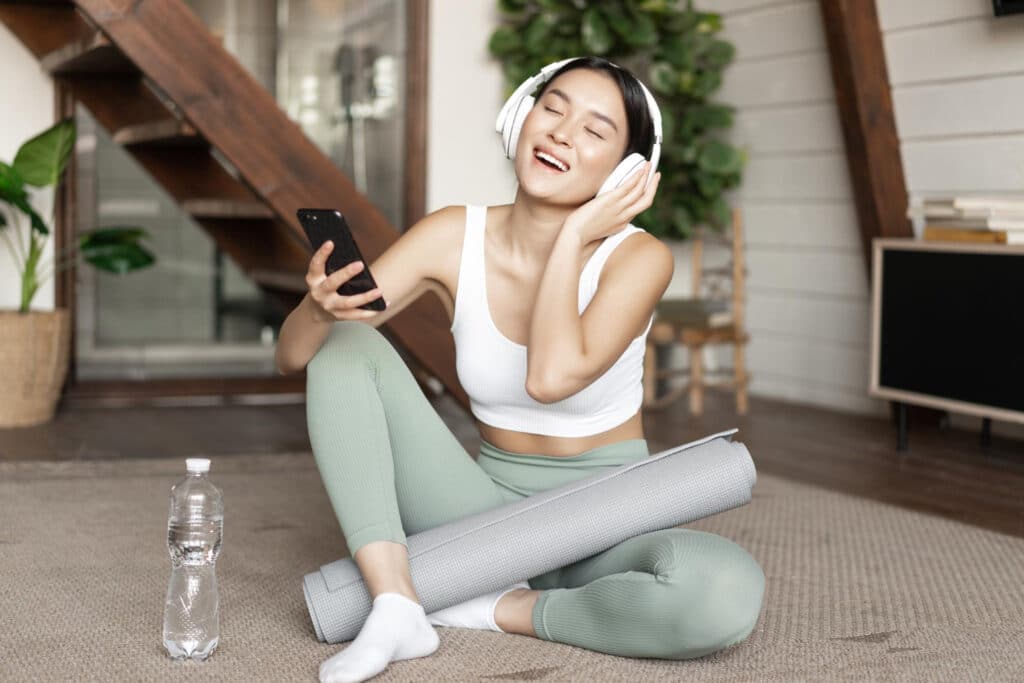 Mulher asiática sentada com fone de ouvido e tapete de yoga