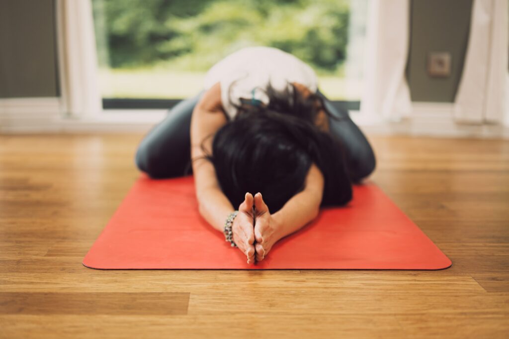 Mulher praticando uma pose de yoga sobre um tapete vermelho.