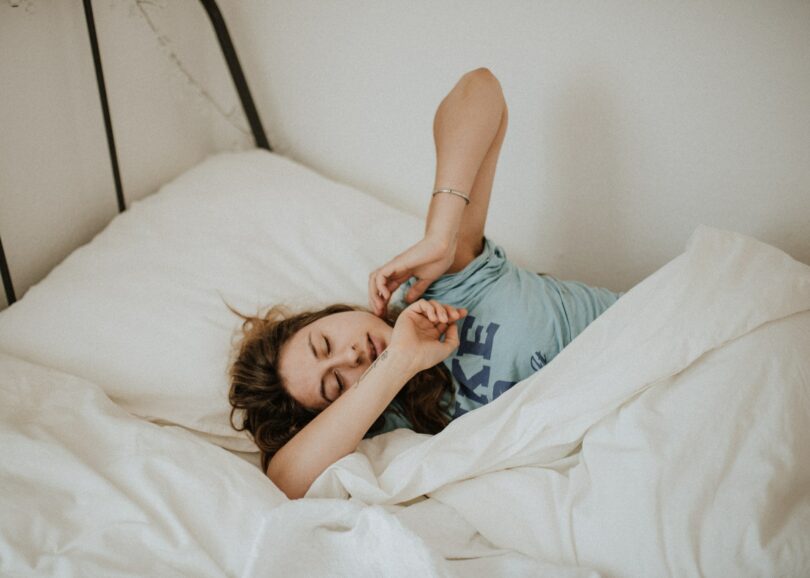 Jovem mulher deitada na cama, entre os lençóis.