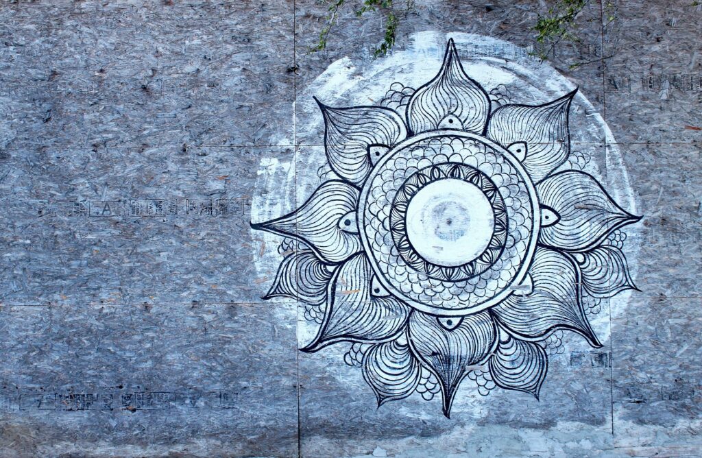 Mandala circular pintada em superfície de madeira, em tons de branco e azul.