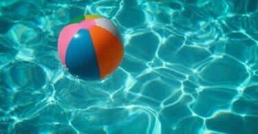 Piscina com água azul e límpida, refletindo, com uma bola colorida boiando sobre a água.