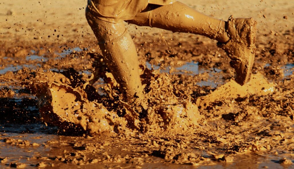 Pernas correndo no meio de um lamaçal, completamente sujas de lama