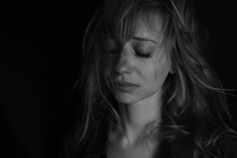 Foto em preto e branco de uma garota chorando, com semblante triste