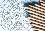 Mandala desenhada em papel com alguns lápis coloridos sobre a folha