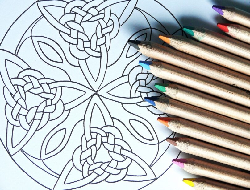 Mandala desenhada em papel com alguns lápis coloridos sobre a folha