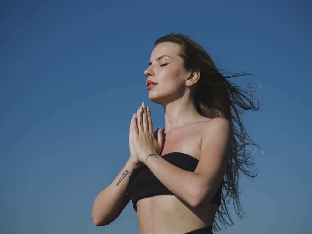 Mulher de olhos fechados e com as mãos no peito, como se estivesse meditando ou orando