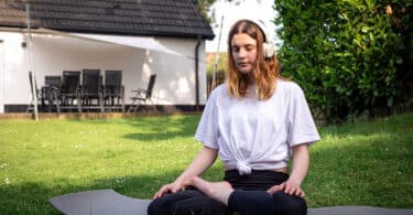 Menina em meio a natureza com fones de ouvido fazendo yoga