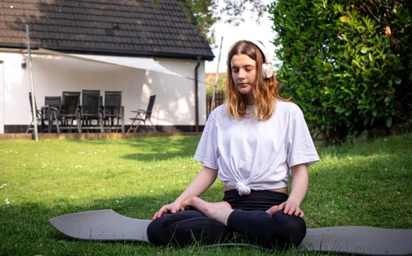 Menina em meio a natureza com fones de ouvido fazendo yoga