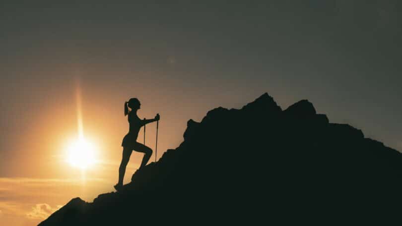 Imagem de uma mulher escalando uma montanha ao pôr do sol