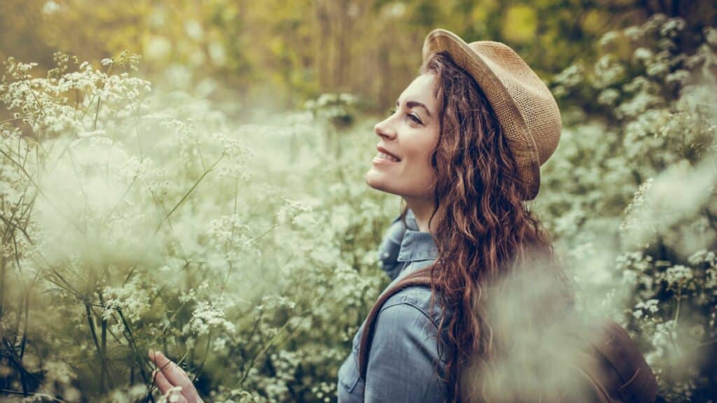 Imagem de uma mulher sorrindo e olhando para o alto no meio de um campo de flores.