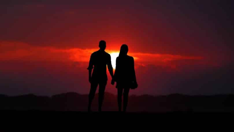Imagem de um casal d emãos dadas e atrás deles o pôr do sol