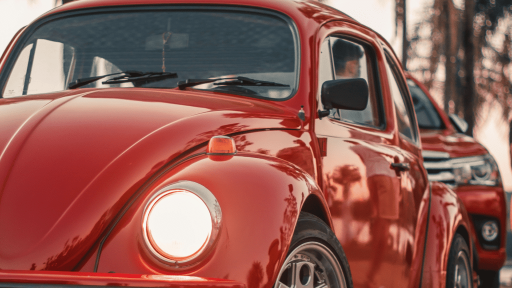 Imagem de um fusca vermelho e a ponta de um carro mais novo atrás.