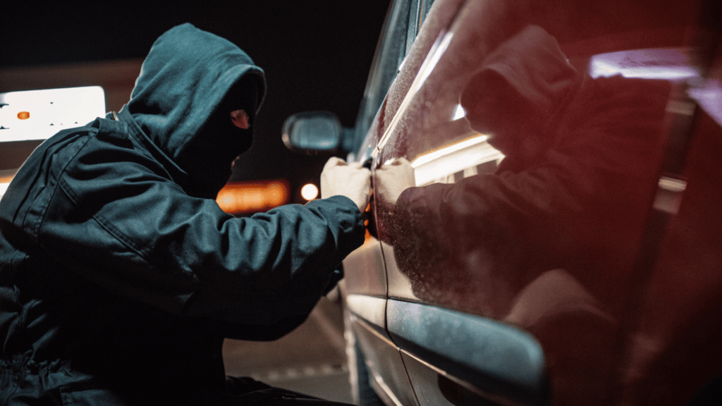 Homem de capuz e máscara roubando carro vermelho