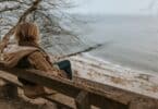 Mulher sentada em um banco, olhando o mar, em um dia nublado e frio.