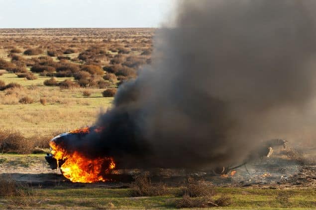 Carro pegando fogo no meio da estrada, coberto por fumaça preta