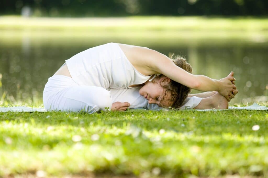 Mulher fazendo Yoga ao ar livre, numa grama verde