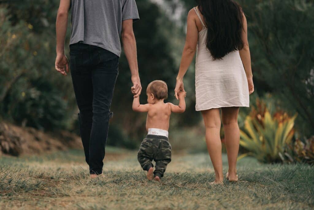 Casal caminhando de mãos dadas com seu bebê.