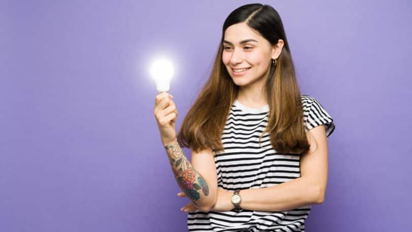 Imagem de uma mulher segurando uma lâpada acesa (de forma ilustrativa) e sorrindo.