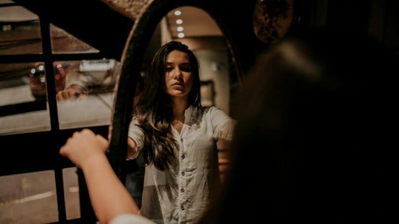 Imagem de uma mulher refletida no espelho com a feição pensativa