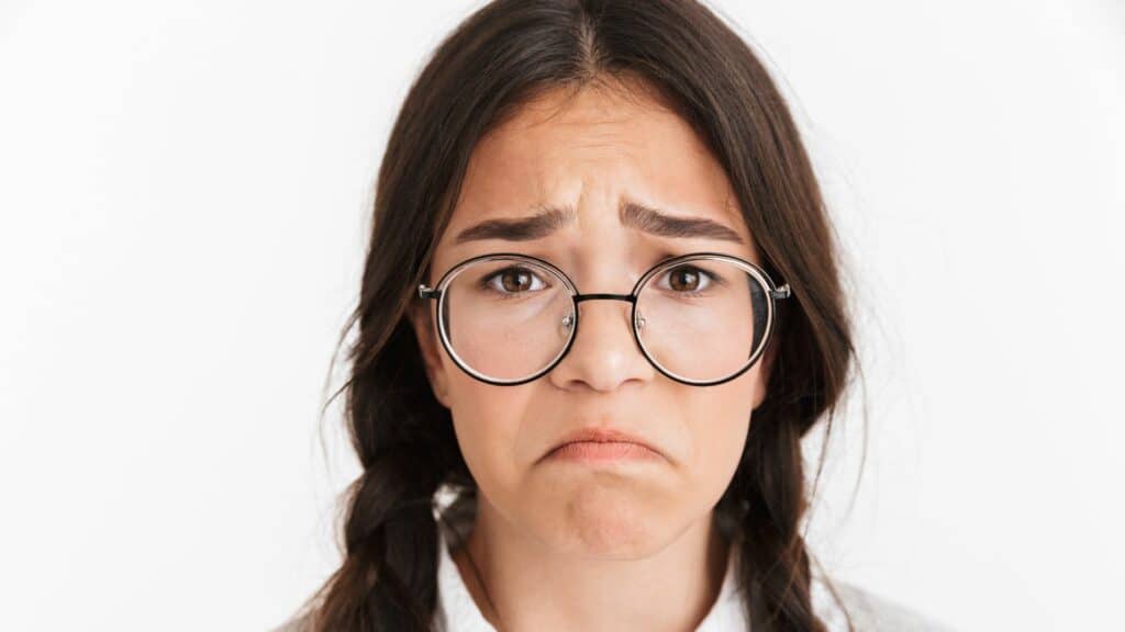 Imagem de uma moça de óculos com a expressão triste (de forma cômica)