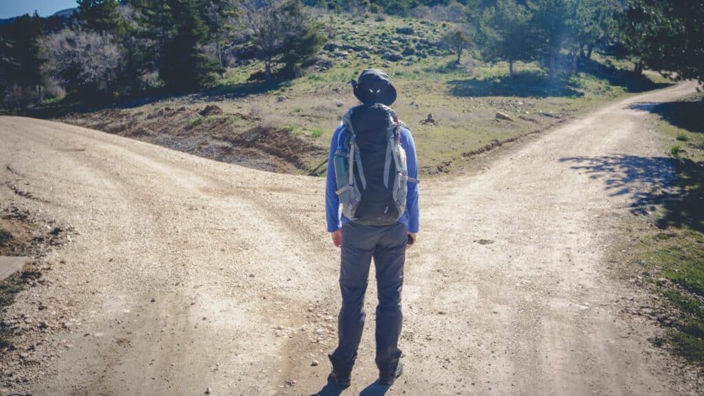 Imagem de um homem diante de dois caminhos na estrada de terra, como se tivesse que decidir qual escolher