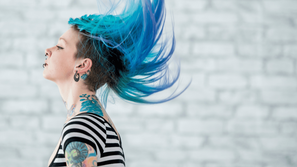 Mulher branca com cabelo raspado na lateral e azul, com piercings e tatuagens, do estilo punk