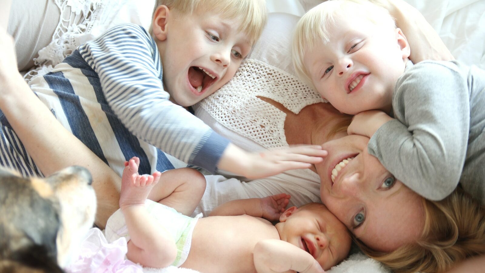 Happy Young Mother And Three Children Snuggling On Bed