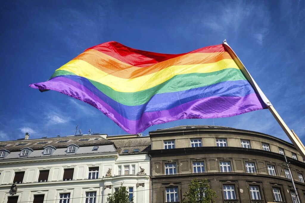 Bandeira LGBTQIAP+ hasteada sob um céu azul na cidade
