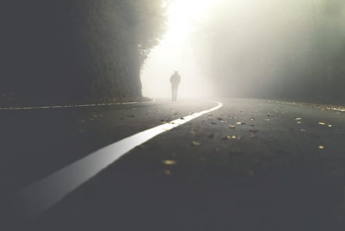 Silhueta de uma pessoa caminhando, ao longe, em uma estrada nebulosa.