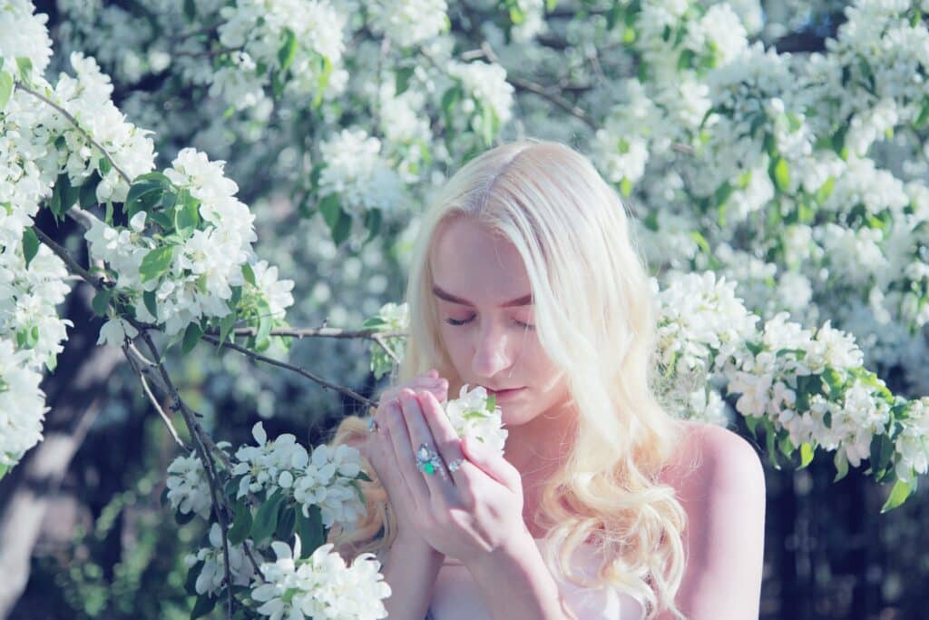 Mulher entre várias flores brancas, segurando algumas nas mãos e sentindo seu cheiro.