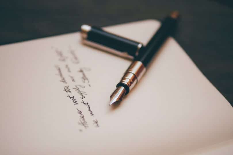 Caneta aberta sobre um caderno com algo escrito.
