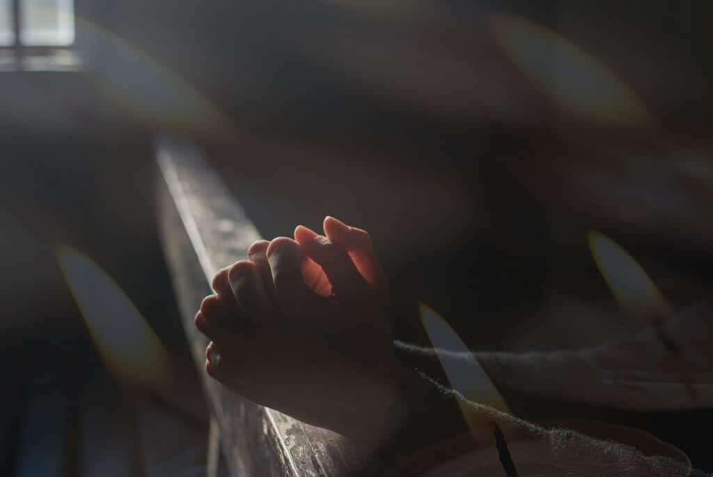 Mãos rezando em ambiente escuro