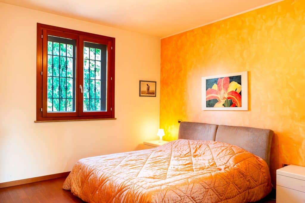 Quarto dormitório de parede laranja e colcha laranja na cama de casal