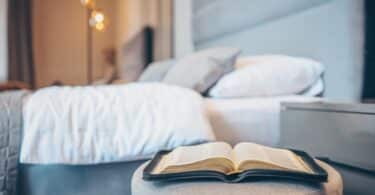 Bíblia em primeiro plano num banco na frente de uma cama de casal