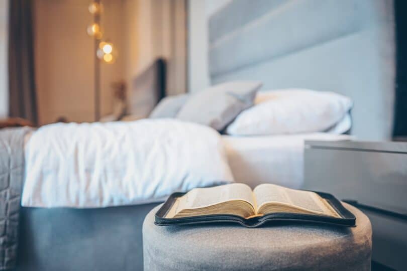 Bíblia em primeiro plano num banco na frente de uma cama de casal