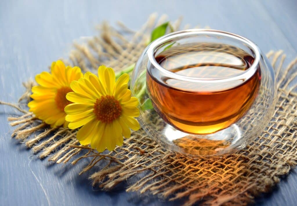 Chá de calêndula em pote de vidro ao lado de flores de calêndula sobre uma mesa