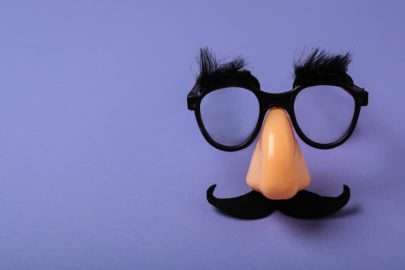 Óculos de disfarce, com bigode e nariz falso, sobre um plano roxo.