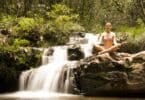 Imagem de uma mulher sentada perto de uma cachoeira fazendo Yoga