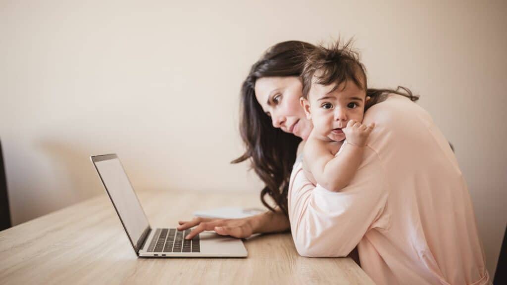 Imagem de uma mãe segurando seu bebê enquanto trabalha na frente do computador.