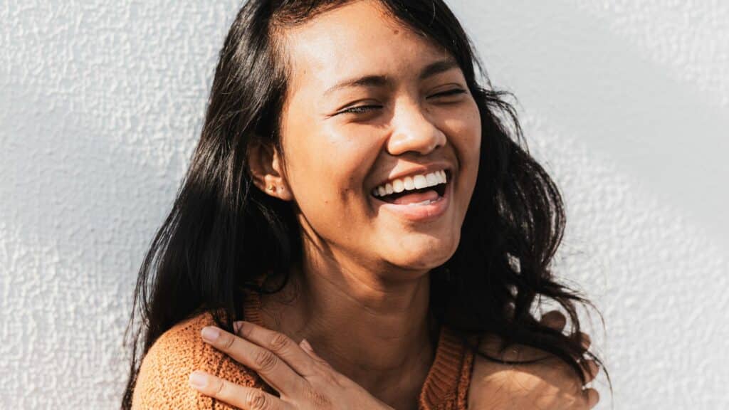 Imagem de uma mulher sorrindo e abreaçando a si mesma de olhos fechados, com expressão de felicidade
