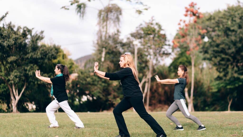 Imagem de três pessoas praticando Tai Chi Chuan ao ar livre