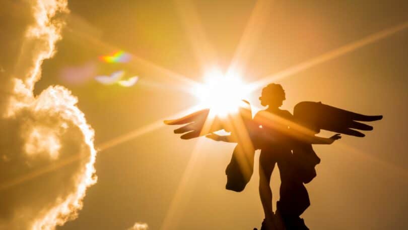 Imagem de um anjo e nele o reflexo do sol em um céu alaranjado
