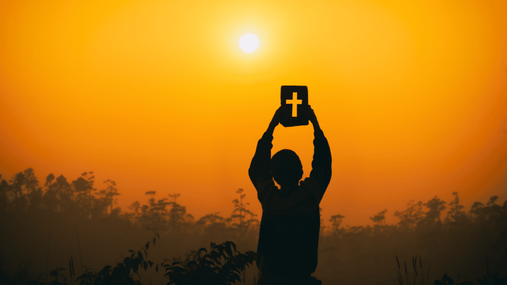 Silhueta de pessoa segurando um papel com forma de cruz, com céu alaranjado ao fundo