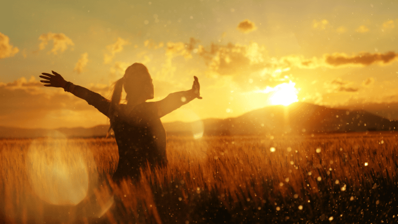 Mulher de braços abertos em meio a natureza sob a luz do pôr do sol