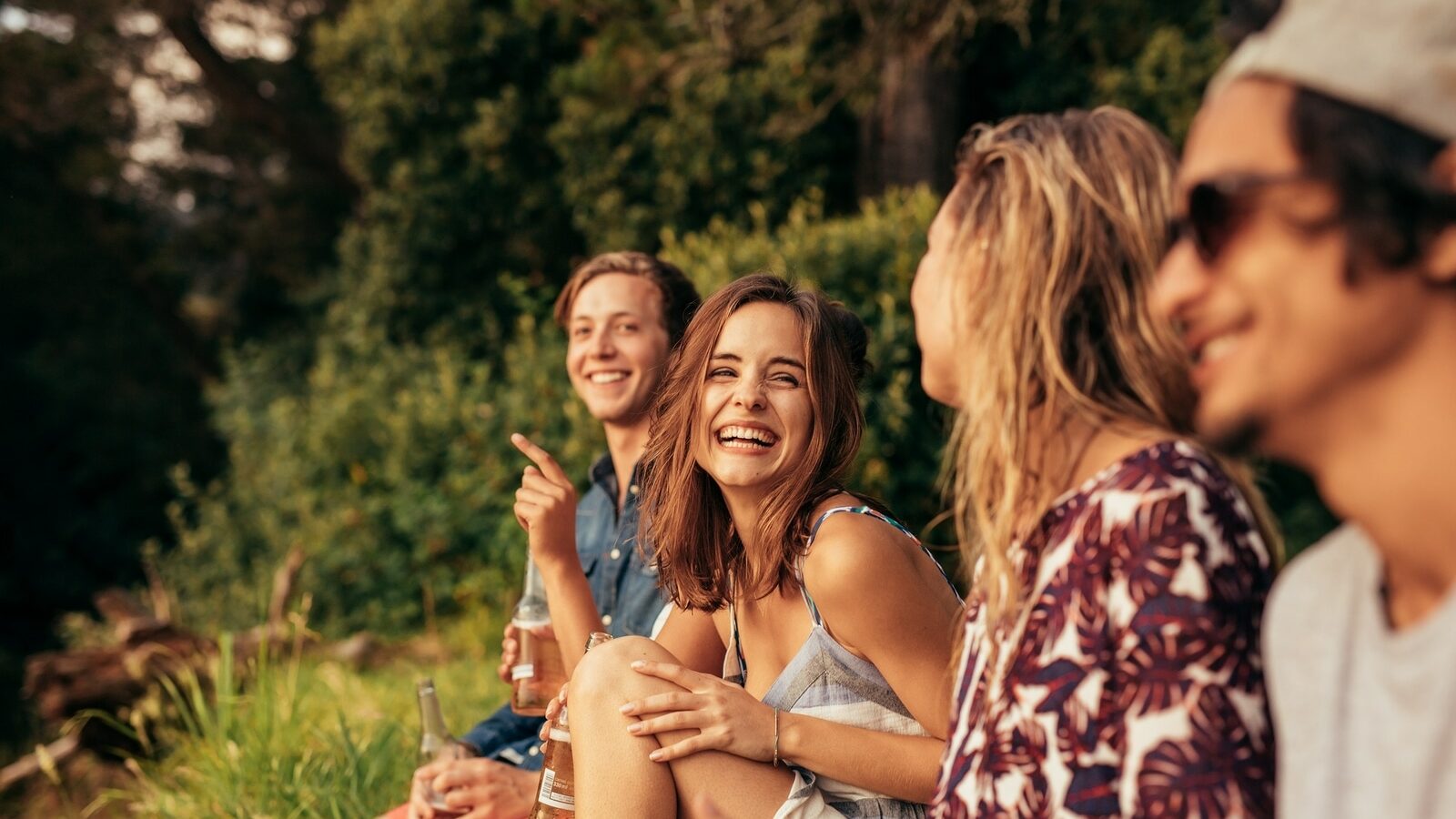 Portrait of cheerful young friends hanging out with beers. Group of friends sitting outdoors and having fun.