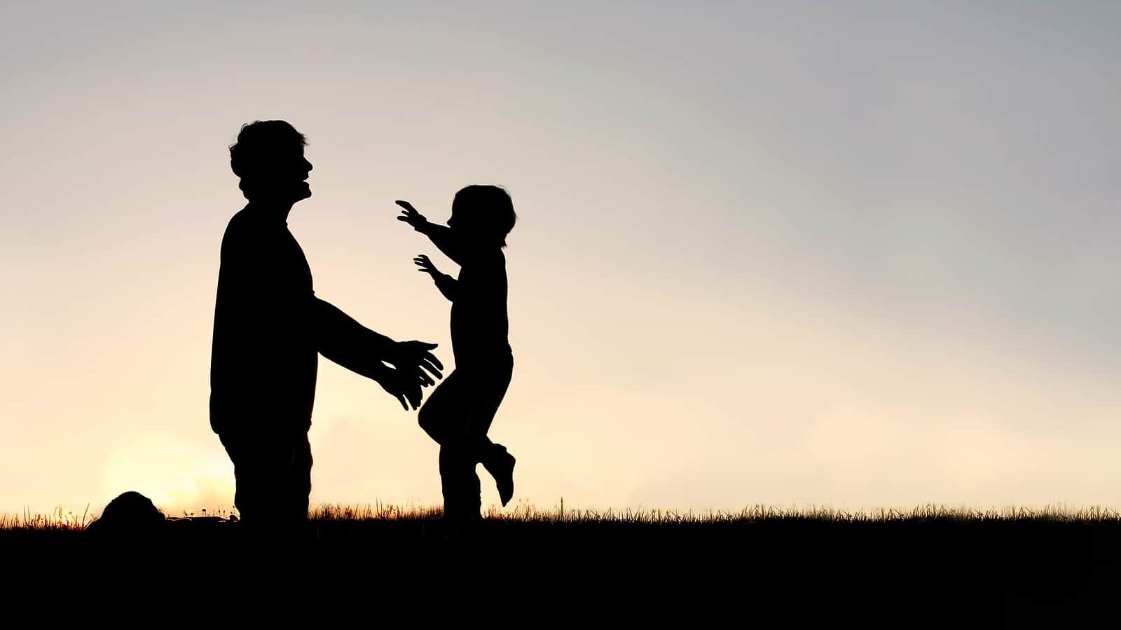 Silhouette of a happy young child smiling as he runs to greet his father with a hug at sunset on a summer day.