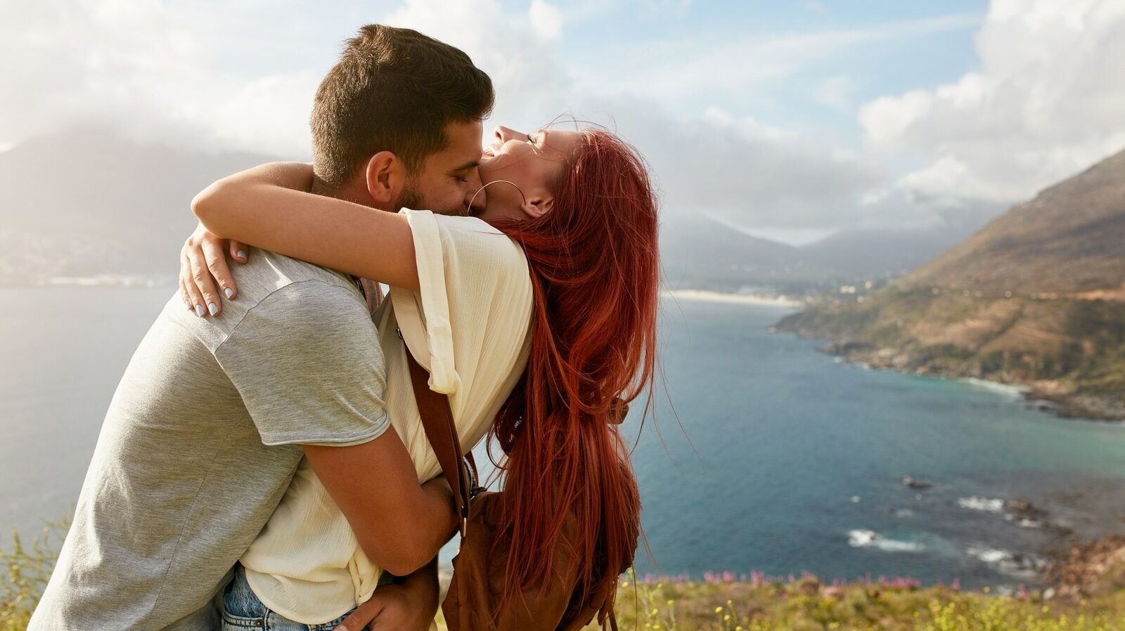 Loving young couple embracing and kissing on a summer day outdoors. Man hugging his girlfriend. Enjoying their summer vacation.