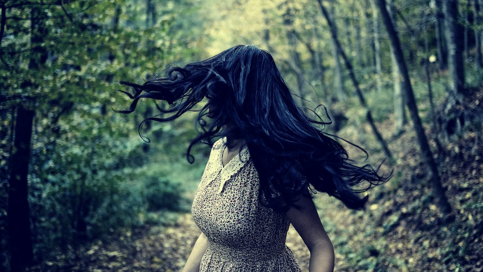 Scared young woman running through a forest at night looking back